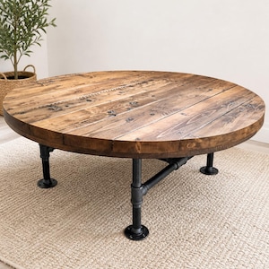 May include: A round coffee table with a rustic design. The tabletop is made of reclaimed wood, and the base is constructed from black metal pipes. The table is approximately 48 inches in diameter and stands about 18 inches tall.
