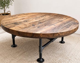 May include: A round coffee table with a rustic design. The tabletop is made of reclaimed wood, and the base is constructed from black metal pipes. The table is approximately 48 inches in diameter and stands about 18 inches tall.
