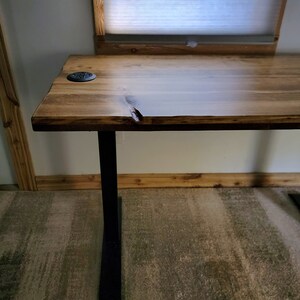 May include: A wooden desk with a live edge top and black metal legs. The desk has a natural wood finish and is sitting on a patterned carpet.