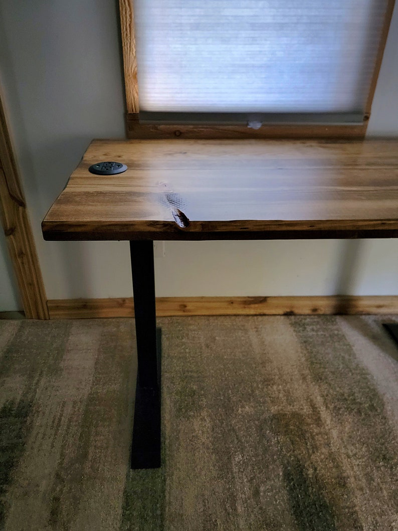 May include: A wooden desk with a live edge top and black metal legs. The desk has a natural wood finish and is sitting on a patterned carpet.