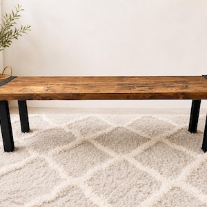 May include: A rustic wooden bench with a rich brown finish. The bench features black metal legs and corner brackets. The design is simple and modern, suitable for various interior styles. The bench is approximately 60 inches long.