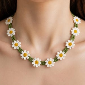 May include: A handmade crochet necklace featuring white daisy flowers with yellow centers, strung on a green crocheted band. The floral necklace is a delicate piece of jewelry.