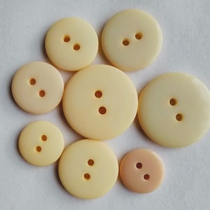 Puede incluir: Surtido de siete botones de dos agujeros en varios tamaños. Los botones son de color crema con un acabado liso y ligeramente brillante.