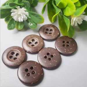 Könnte beinhalten: Sechs braune Kokosnuss-Knöpfe mit jeweils vier Löchern. Die Knöpfe sind in einem Kreis auf einer hellbraunen Oberfläche angeordnet.