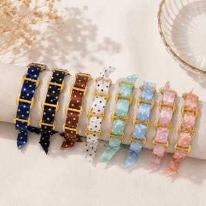 Peut inclure: Une collection de huit bracelets composés de rubans en satin à pois blancs enfilés dans des maillons en métal doré. Les bracelets sont présentés en rangée, déclinés en bleu marine, noir, marron, blanc, menthe, bleu clair, rose et pêche.