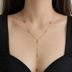Peut inclure: Un collier lariat doré composé d'une chaîne fine agrémentée de petites perles régulièrement espacées et de six maillons ovales avec une barre horizontale. Le collier présente un design en Y avec une section de chaîne verticale centrale.