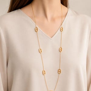Peut inclure: Un long collier doré avec des maillons ovales espacés sur une chaîne fine. Le collier est présenté sur un fond neutre, soulignant son design élégant. Le collier est un bijou.