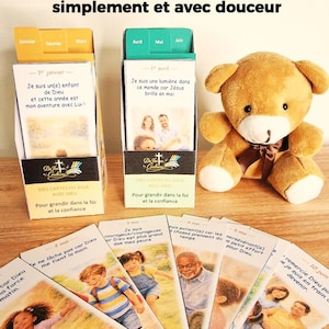 Op de afbeelding: Een bruine teddybeer zit naast twee kaarthouders en verschillende kaarten. De kaarthouders hebben Franse tekst. De kaarten bevatten illustraties van kinderen en volwassenen met inspirerende boodschappen.