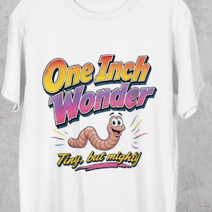 Op de afbeelding: Wit t-shirt met een cartoon worm ontwerp. De tekst "One Inch Wonder" staat in een kleurrijk retro lettertype, met "Tiny but mighty!" eronder. De worm is lichtbruin en lacht.