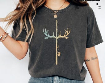 May include: A charcoal grey short-sleeve t-shirt featuring a graphic print of a cross formed by a fishing rod and deer antlers. The design is rendered in a distressed, muted gradient of blue, yellow, and orange tones centred on the chest.