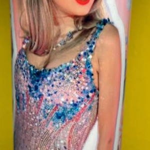 May include: A cylindrical tumbler featuring a photographic print of a person with shoulder-length hair wearing a sequined bodysuit in shades of pink and blue. The design includes heart-shaped sunglasses and the text "daylight" in cursive script.