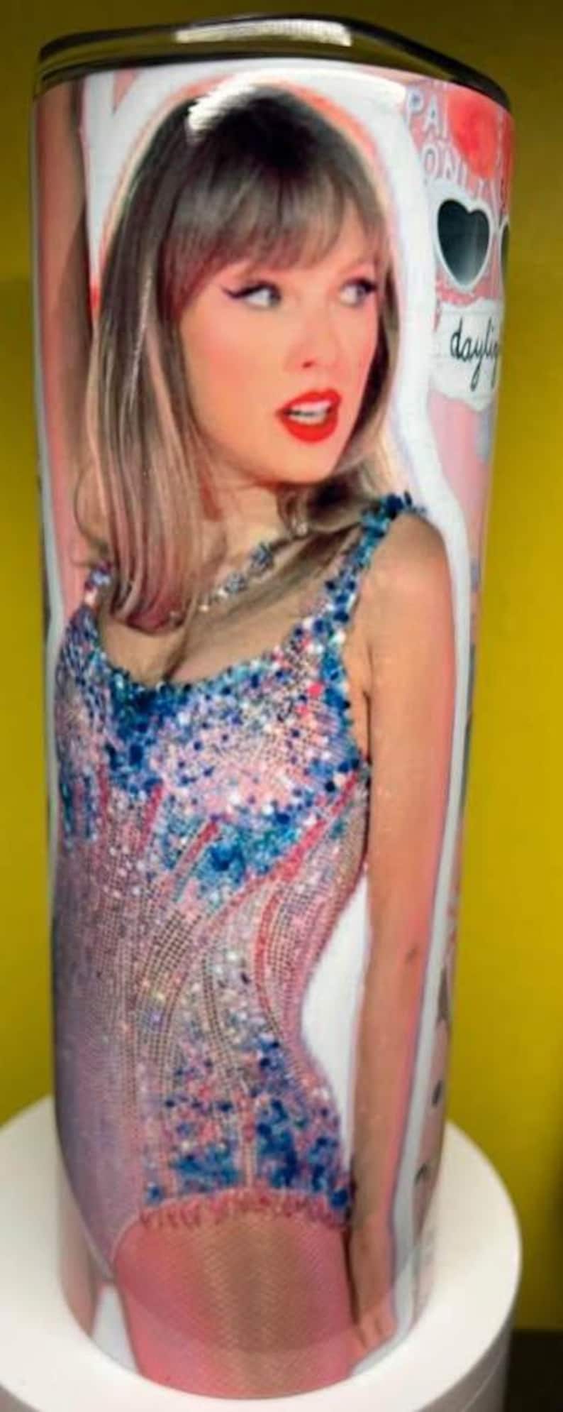 May include: A cylindrical tumbler featuring a photographic print of a person with shoulder-length hair wearing a sequined bodysuit in shades of pink and blue. The design includes heart-shaped sunglasses and the text "daylight" in cursive script.