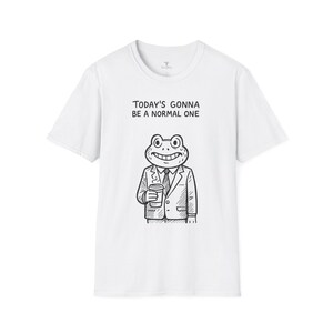 May include: White t-shirt featuring a cartoon frog in a suit holding a coffee cup. The text "TODAY'S GONNA BE A NORMAL ONE" is printed above the frog illustration. The shirt has a crew neck and short sleeves.