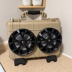 May include: Tan portable speaker system with two black speakers. The speakers are mounted on a tan case with a handle. The system has black feet for stability. Above the speaker system are two white ceramic containers labeled "SALT" and "PEPPER".