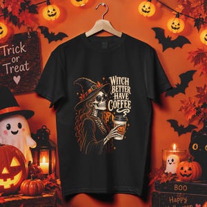 May include: A black short-sleeve t-shirt featuring a graphic of a skeleton wearing a witch hat and sunglasses, holding a coffee cup. The text reads Witch Better Have Coffee. The design uses orange, yellow, and white colors on the black fabric.