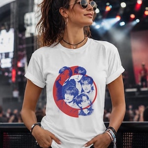 May include: A white short-sleeved t-shirt featuring a circular graphic print in red and blue. The design displays a collage of five individuals in a blue monochromatic style, layered over a solid red circle that is partially cut off on the left side.
