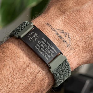 Op de afbeelding: Een medische alarmarmband met een zwarte rechthoekige metalen plaat, het witte Ster van Leven-symbool en gegraveerde tekst: Keep, Type 2 Diabetes, Allergy, Penicillin, ICE: Chris 123-456-7890, Sarah 098-765-4321, See Wallet for Meds. Olijfgroene gevlochten band.
