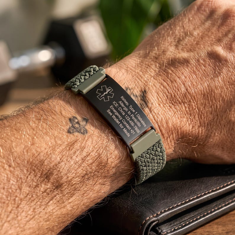 May include: An olive green woven medical alert bracelet featuring a black metal plate with the Star of Life symbol and engraved text: Kelsey, Type 1 Diabetes, Allergic to Penicillin, ICE: Chris 123-456-7886, Emergency Contact +21, See Wallet for Meds.