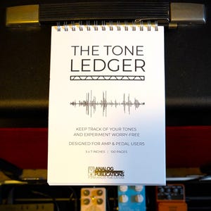 May include: A white spiral-bound notebook titled "THE TONE LEDGER" with black text and a sound wave graphic. The notebook is 5x7 inches and has 100 pages. It is designed for amp and pedal users.