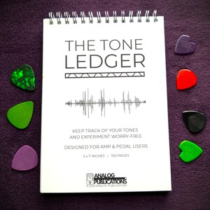 May include: A spiral-bound notebook titled "THE TONE LEDGER" with a sound wave graphic, designed for amp and pedal users. The notebook is 5 x 7 inches and has 100 pages. Six guitar picks in various colors surround the notebook on a purple surface.