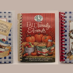 May include: Three spiral-bound cookbooks titled Seasons for Sharing, Fall Family & Friends, and The Cozy Home Cookbook. Each book features a Gooseberry Patch logo, colorful illustrations of food, seasonal decor, and text on the front covers.