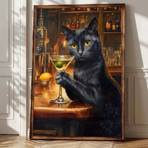 Op de afbeelding: Een ingelijste muurkunstprint met een zwarte kat met gele ogen die aan een houten bar zit. De kat houdt een martiniglas met een groene olijf vast. Op de achtergrond staan planken vol met diverse glazen flessen en glaswerk.