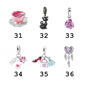 May include: A collection of six silver charms labeled 31 through 36. The charms feature a pink teacup, a black cat, a pink seashell, a fish bone with a cat and paw print, a red shoe with a handbag and dress, and a heart-shaped dreamcatcher.