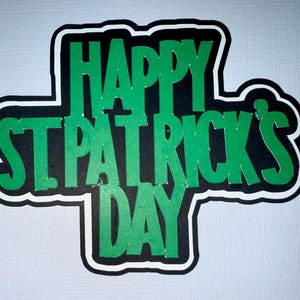 May include: A St. Patrick's Day decoration with the words "HAPPY ST. PATRICK'S DAY" in green. The text is outlined in black and white, set against a black background. A festive design for the Irish holiday.