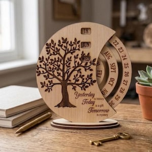 Könnte beinhalten: Ein runder, hölzerner ewiger Kalender mit einem lasergravierten Baumdesign und drehbaren Ringen für Datum, Monat und Wochentag. Der Text lautet: Yesterday is history, Today is a gift, Tomorrow is mystery. Er zeigt 18, JUN und WED an.