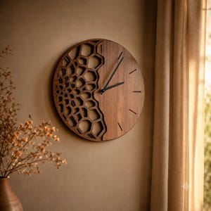 Puede incluir: Un reloj de pared circular de madera con un acabado de veta de madera marrón oscuro. El lado izquierdo muestra un intrincado patrón de panal cortado con láser, mientras que el lado derecho es sólido con marcadores de hora y manecillas negras.