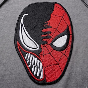 May include: A grey short-sleeved t-shirt featuring a large embroidered patch on the chest. The patch depicts a split face design, with one side black showing a white eye and sharp teeth, and the other side red with a black web pattern and white eye.