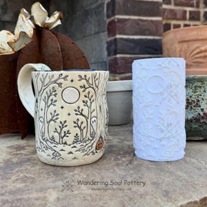 May include: A cream-colored ceramic mug featuring a black ink illustration of a forest with ghosts, stars, and a small orange pumpkin, alongside a white cylindrical silicone mold embossed with a detailed woodland pattern and a circular moon shape.