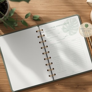 Può includere: Quaderno aperto con copertina verde e rilegatura a spirale dorata, con il testo "FICHE ADMINISTRATIVE" e un disegno a foglia di monstera. Una penna d'oro e una tazza di caffè sono posizionate su una superficie di legno. Il quaderno è aperto su una pagina bianca.