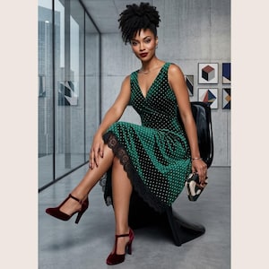 May include: A sleeveless emerald green velvet dress featuring a white polka dot pattern, a V-neckline, and a black lace trim along the hemline. The dress is paired with dark red velvet T-strap heels and a small geometric patterned clutch bag.