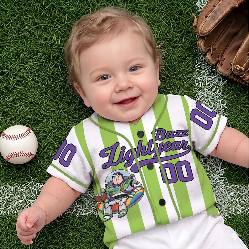 Może przedstawiać: Niemowlę w biało-zielonej koszulce baseballowej w paski z napisem "Buzz Lightyear" i numerem "00" w kolorze fioletowym. Na zdjęciu znajduje się r&oacute;wnież piłka do baseballu i rękawica do baseballu.