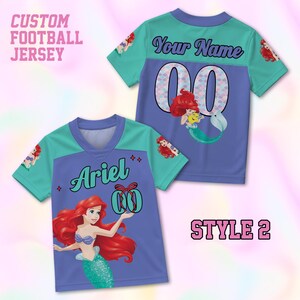 Puede incluir: Camiseta de f&uacute;tbol personalizada en el estilo 2, con un cuerpo morado y mangas y cuello turquesa. La camiseta muestra el nombre "Ariel" y el n&uacute;mero "00" con un gr&aacute;fico de sirena. El texto "CUSTOM FOOTBALL JERSEY" es visible.