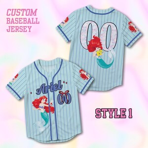May include: Pale blue baseball jersey with vertical stripes, displaying the name "Ariel" and the number "00" with a mermaid illustration. The jersey has short sleeves and a button-up front. The text "CUSTOM BASEBALL JERSEY" and "STYLE 1" are also visible.