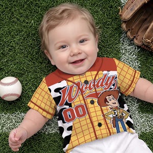 Puede incluir: Una camiseta de b&eacute;isbol de manga corta con botones, con un patr&oacute;n de cuadros amarillos, detalles de estampado de vaca en blanco y negro, y un gr&aacute;fico del personaje Woody. El frente muestra el texto Woody's y el n&uacute;mero 00 en letras rojas y azules.