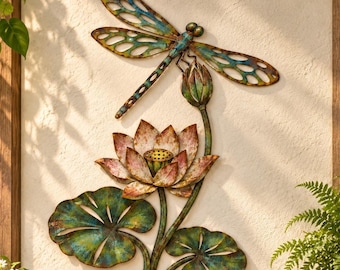Può includere: Un'opera d'arte da parete in metallo raffigurante una libellula con ali traforate nei toni del blu e del bronzo, appoggiata sopra un fiore di loto in fiore con petali rosa e verdi, su grandi foglie di ninfea verdi e testurizzate.