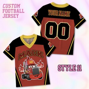 May include: A custom football jersey featuring a red and black design with yellow trim. The front displays a cartoon truck graphic with the text MACK and flames. The back shows the text YOUR NAME and the number 00. Text reads CUSTOM FOOTBALL JERSEY.