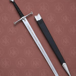 Op de afbeelding: Een zilverkleurig stalen zwaard met een zwart lederen handvat, een kruisvormige pareerstang en een pommel met een goudkleurige inleg. Het lemmet bevat geëtste tekst en een stersymbool. Een bijpassende zwarte schede met zilveren metalen beslag is inbegrepen.