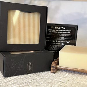 Op de afbeelding: Een rechthoekig stuk talkzeep met citroengras, verpakt in een zwarte doos met een venster. Het etiket vermeldt DEXTER VEISERASVA SEEP SIDRUNHEINAGA / TALLOW SOAP WITH LEMONGRASS, met een nettogewicht van 125 gram en batchnummer 1025.