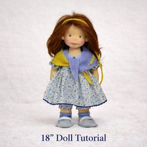 May include: A handmade doll, approximately 18 inches tall, with red hair and a yellow headband. The doll wears a blue and yellow shawl, a floral print dress, and matching pants. The doll is wearing gray shoes and blue and white striped socks. The text "18" Doll Tutorial" is at the bottom.