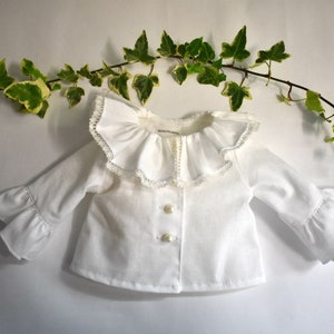A collage of six doll clothing items. Top left: white blouse with wide lace collar and pearl buttons. Top right: linen overalls with orange puff-sleeve shirt. Center: long-sleeve floral dress in navy with pink and orange flowers. Bottom right: denim jeans with front pockets. Small inset photos show a white romper and an orange off-shoulder blouse. All designed for 18" dolls.