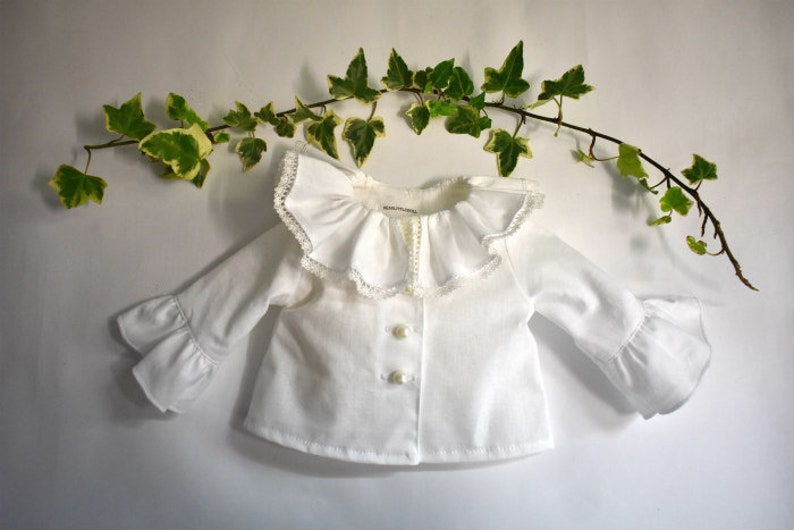 A collage of six doll clothing items. Top left: white blouse with wide lace collar and pearl buttons. Top right: linen overalls with orange puff-sleeve shirt. Center: long-sleeve floral dress in navy with pink and orange flowers. Bottom right: denim jeans with front pockets. Small inset photos show a white romper and an orange off-shoulder blouse. All designed for 18" dolls.