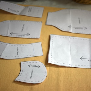 May include: A set of six sewing patterns for a craft project. The patterns are printed on white paper and have dashed lines around the edges. The patterns are labelled with instructions for cutting and sewing.