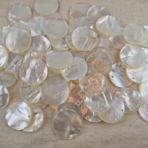 May include: A collection of round, flat mother-of-pearl shell discs, each featuring a single small hole near the edge. These iridescent, off-white circular pieces display a natural, glossy finish with subtle variations in texture and light reflection.