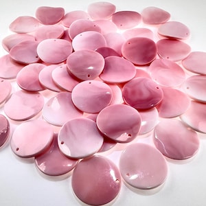 May include: A collection of numerous circular, flat, pink shell-like beads with smooth, glossy surfaces. Each bead features a single small hole near the edge for threading. The shades of pink vary from pale pastel to deeper rose, with subtle marbled patterns.