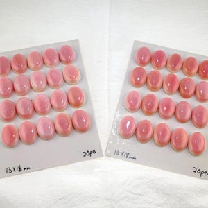 May include: Two white display cards each holding 20 oval-shaped pink cabochons. Each card features the handwritten text 13x18 mm and 20pcs. The smooth, polished pink stones are arranged in four rows of five on each rectangular card.