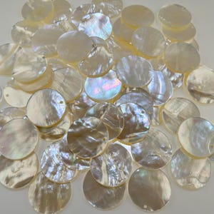 May include: A collection of circular mother of pearl shell discs, each featuring a smooth, iridescent surface with natural pearlescent white and cream tones. These flat, round components include small pre-drilled holes for threading or attachment.